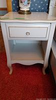 Front view of white side table showing drawer and lower shelf on red carpet