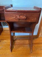 Pair of reddish-brown wooden side tables showing top, drawer, curved legs and lower shelf with visible scratches and wear.