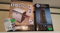 Photo showing HP film slide and photo converter packaging alongside HP Essential USB Port Replicator box, with a price tag and item label visible.