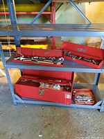 Wide angle view of four red metal toolboxes on metal shelving. Boxes contain various sockets, wrenches, and hand tools.