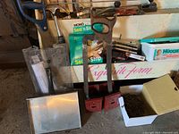 Photo showing hand saws, two red clamps, a metal stapler and a box of nails.