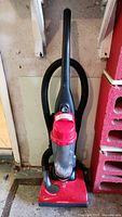 Full view of red Dirt Devil Featherlite upright vacuum cleaner with hose attached, standing on floor.