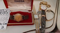 Omega box containing gold-tone dial watch on leather strap alongside other watches