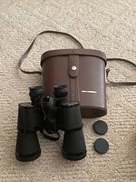 Bell & Howell binoculars with carry case and lens caps on carpeted floor.