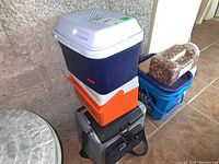 Stack of three small coolers: Rubbermaid, Coleman, Arctic Zone. Two coolers have handles, one cooler has a carry strap.
