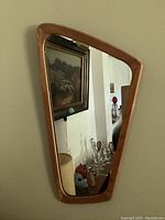 Full view of asymmetrical wooden framed mirror hung on wall showing shape and frame finish.