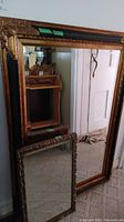 Two framed decorative mirrors leaning against a wall, showing sizes and ornate frames