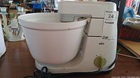Side view of Braun mixer showing large white plastic mixing bowl, control dial, and power cord.
