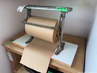 Front view showing the metal frame holding the brown paper roll on a wooden base, with paper roll partially unrolled downwards.