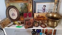 View of entire shelf showing multiple framed prints, brass pot, glass lamp base, small bookend, and other small collectibles arranged together