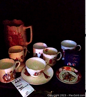 Photo showing a large pitcher, four mugs, a small plate, and two saucers with British Royalty themed decorations.