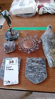 Five items displayed on a wooden surface: soapstone seal, soapstone frog, soapstone Canada plaque, metal filigree dish with copper center, and a figurine on soapstone base.