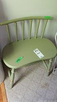 Green painted wood stool with crescent-shaped seat, spindle backrest with gold accents, and rounded legs, showing some paint chips and scratches.