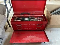 Open red metal toolbox showing three drawers labeled for different tools and the top compartment containing various hand tools including pliers and snips.