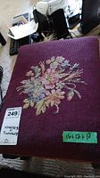 Detailed top view of the footstool showing the needlepoint floral embroidery on burgundy fabric.