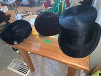 Three vintage hats displayed on a wooden table showing details and size variation