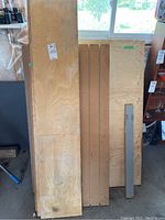 Long pine boards and plywood sheets leaning against a wall with a window in the background.