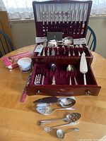 Full view of wooden chest containing sterling silver flatware and serving utensils organized in velvet lined compartments.