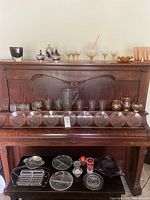 Wide view of glassware, plates, trays, and pitchers displayed on a wooden piano.