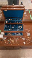 Open wooden jewelry box showing top tier compartments with various small brooches and pins