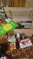 Open wooden trunk showing contents of assorted kids games including Payday, Spirograph, a tall Monopoly-related box, and other smaller game boxes.