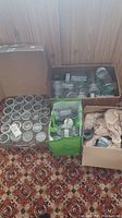 Multiple glass jars grouped in boxes on carpet, some with metal lids, some loose with packing paper