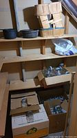 Wide shot showing several boxes of glass jars on lower shelves, wooden baskets and cast iron pots on upper shelves.