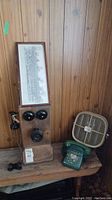 Vintage wood wall phone with black bells, mouthpiece, and receiver on wooden shelf with green rotary phone and Seabreeze fan nearby