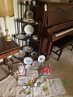 Photo of corner shelf unit with assorted decorative plates arranged on shelves and on floor along with linens.