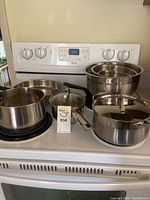 Full view of cookware including saucepans, lids, and bowls on stovetop