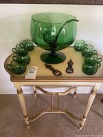 Green glass punch bowl set arranged on light wood table with eight green cups and two metal bottle openers