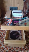 Full view of vintage wooden record player cabinet with open lid and visible vinyl records in a drawer beneath.