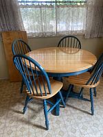 View of round kitchen table with four matching chairs around it, showing natural wood top and blue-painted legs and chair backs.