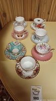Overview of six tea cups with matching saucers arranged on a yellowish surface against a wood paneled background.