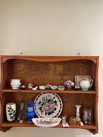 Wide view showing two shelf rows with ceramic vases, floral plates, ceramic flowers, and decorative items
