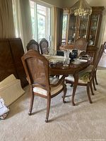 Full view of oval dining table with six cane back chairs and china cabinet in background