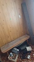 Photo of the solid wood bench positioned against a wood paneled wall, showing its seat and some floor area with other items not included in sale.