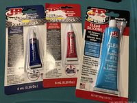 Three tubes of JB Weld adhesives including blue and red Perma-Lock thread lockers and a clear silicone sealant.
