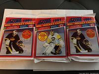 Image showing three unopened and sealed 1991 Score NHL hockey wax packs featuring player illustrations on the fronts and special Bobby Orr card offer noted