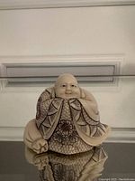 Full image of the Buddha carving showing seated figure with detailed robe and joyful facial expression.