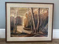 Framed oil on board landscape painting showing trees and a river with autumn colored foliage.