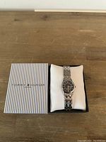 Tommy Hilfiger wristwatch displayed on a white cushion alongside its original striped box on a wooden surface.