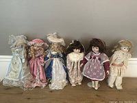 Full view of six porcelain dolls standing in a row showing variety of outfits and hairstyles