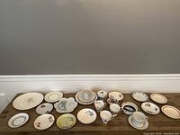 Wide shot showing various porcelain pieces including plates, teacups, saucers, and a butter dish arranged on a wooden table.
