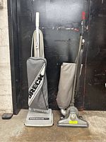 Photo of two vacuum cleaners side by side, an Oreck XL with gray bag and a vintage metal vacuum with beige bag.