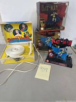 Photo showing the vintage record player with white and yellow plastic casing featuring superhero artwork, and three Classic Batman figurines, two still boxed and one loose on a stand.