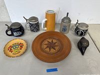 Overview image showing all items on display including four beer steins, two plates, ceramic pitcher, and metal conch shell.
