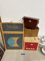 Overall lot including Willamantic camera case on top of its box, Baia branded box, vintage Bell & Howell box, and other boxed items.