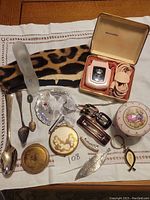 Full lot overview showing shaver, leopard print fabric, compacts, figurine, barrettes, spoons, and pendants.