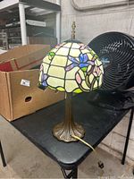 Front and side view of the lamp showing stained glass floral shade and leaf motif metal base.